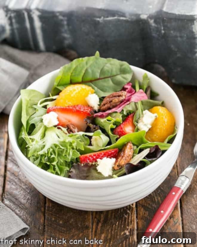 Overhead view of strawberry spinach salad in a white serving bowl, showcasing fresh ingredients like spinach, strawberries, blue cheese, and mandarin oranges.