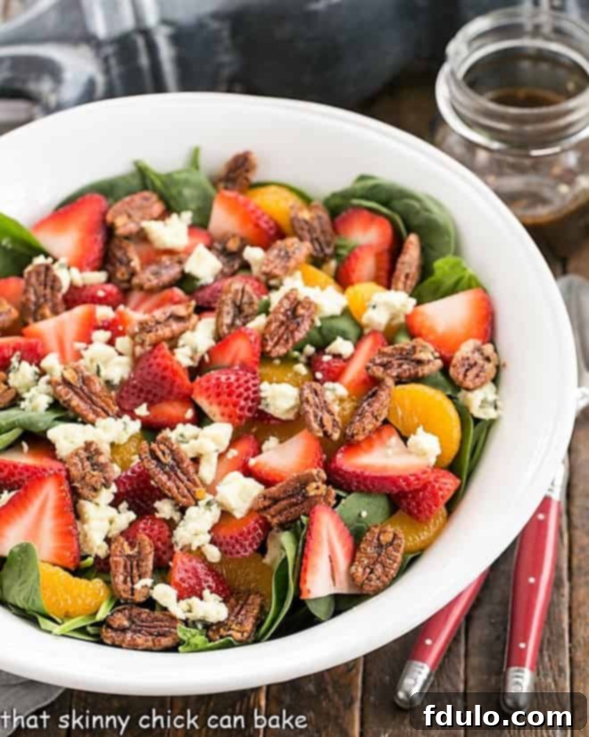 Close-up overhead view of spinach strawberry salad with blue cheese in a white serving bowl, highlighting the texture and vibrant colors of the ingredients.