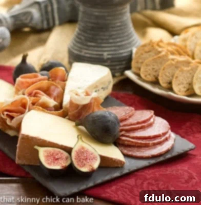 A rustic slate cheese board artfully arranged with a variety of cheeses, thinly sliced cured meats, and fresh garnishes, resting on a crimson linen napkin.