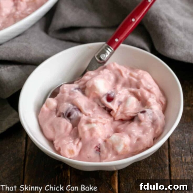 Small white bowl filled with cherry fluff salad with a red handled spoon