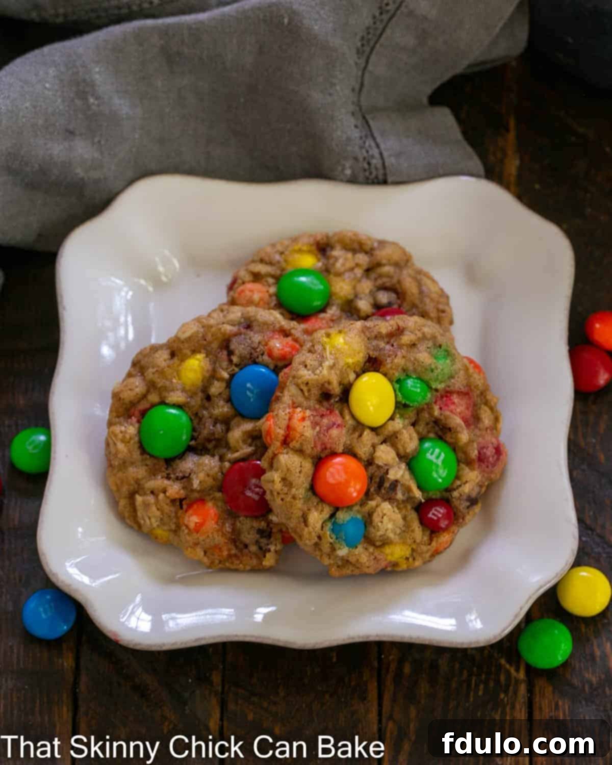 Overhead view of 3 M&M oatmeal cookies on a square white plate.