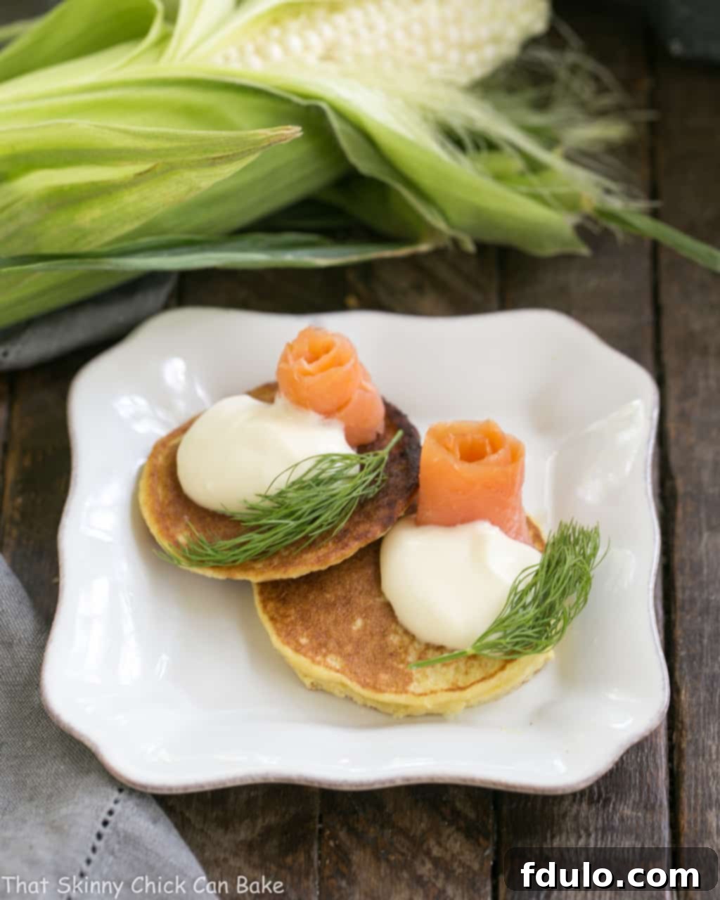 Fresh Corn Pancakes on a square plate, elegantly topped with smoked salmon and fresh dill sprigs.