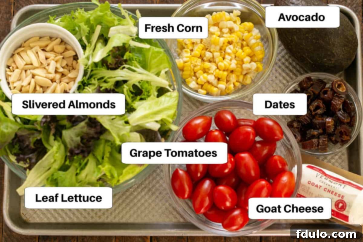 Various fresh ingredients for the Macho Salad laid out on a sheet pan, including corn, tomatoes, dates, and lettuce, with clear labels.