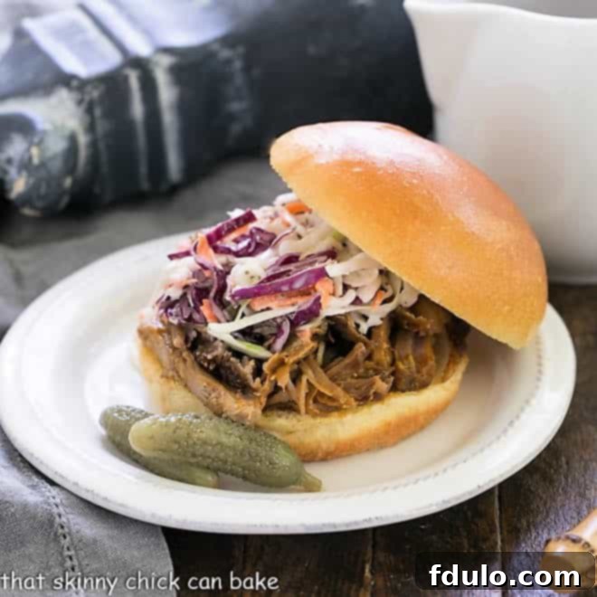 Pulled Pork Sandwich on a bun topped with coleslaw with a pitcher of BBQ sauce