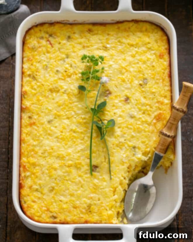 A serving of the freshly baked Fresh Corn Casserole is scooped into a small white bowl, showing its creamy texture and golden top. The casserole looks warm and inviting.