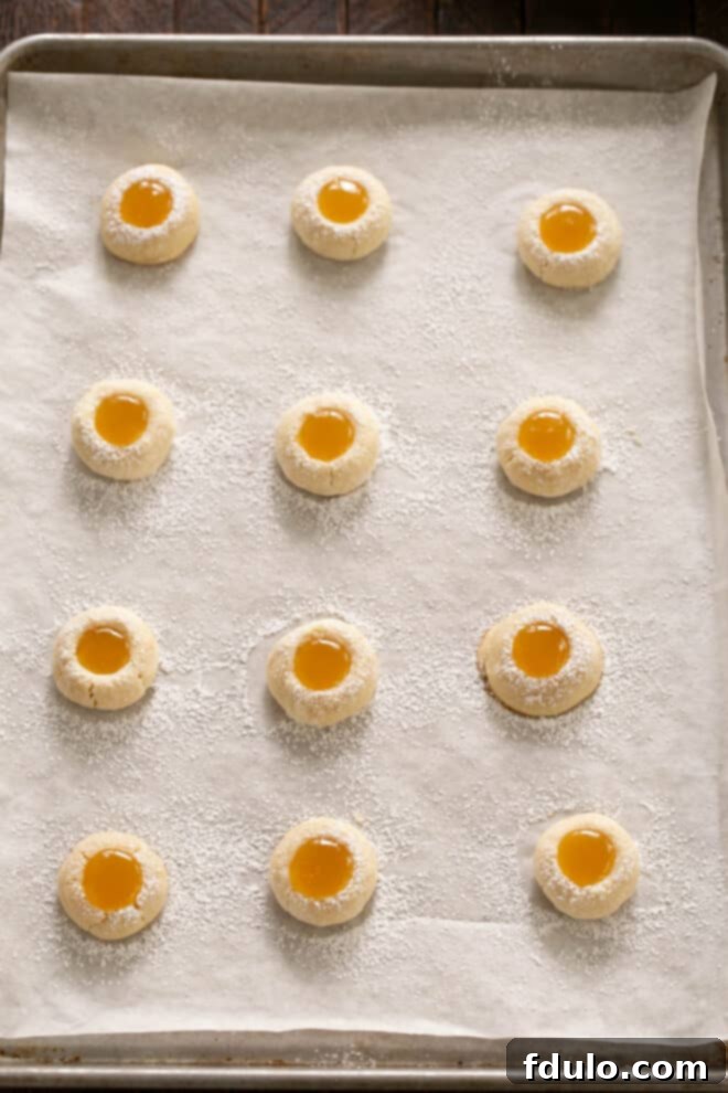 Unbaked thumbprint cookies on a baking sheet, with each divot carefully filled with bright yellow lemon curd.