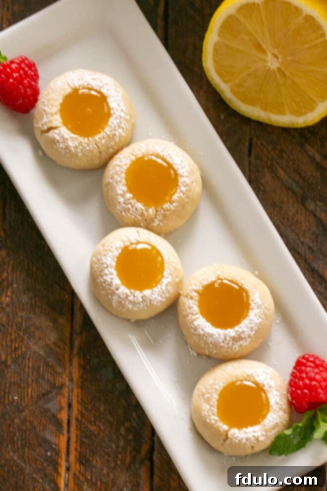 An overhead view of freshly baked lemon thumbprint cookies beautifully arranged on a white tray, showcasing their golden edges and vibrant lemon centers.
