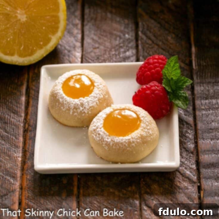 Two exquisite lemon thumbprint cookies arranged on a small square white plate, garnished with fresh raspberries for a touch of color and extra zing.