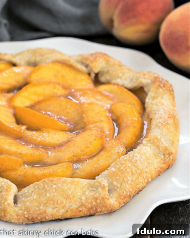 Partial closeup view of a peach galette on a white serving plate, showing the texture of the crust and the glistening peach filling.