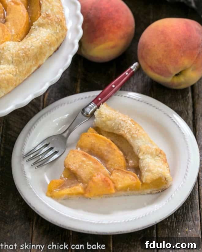 A beautiful slice of peach galette presented on a white plate with a red handle fork, highlighting the juicy filling and flaky crust.