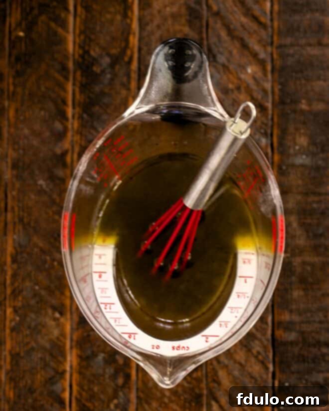 Salad dressing ingredients in a measuring cup with a whisk, ready to be combined.