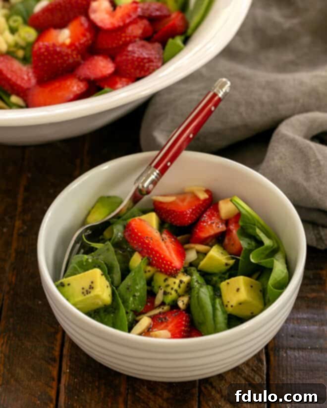 A serving of the colorful strawberry spinach salad with avocado in a bowl with a red-handled fork.