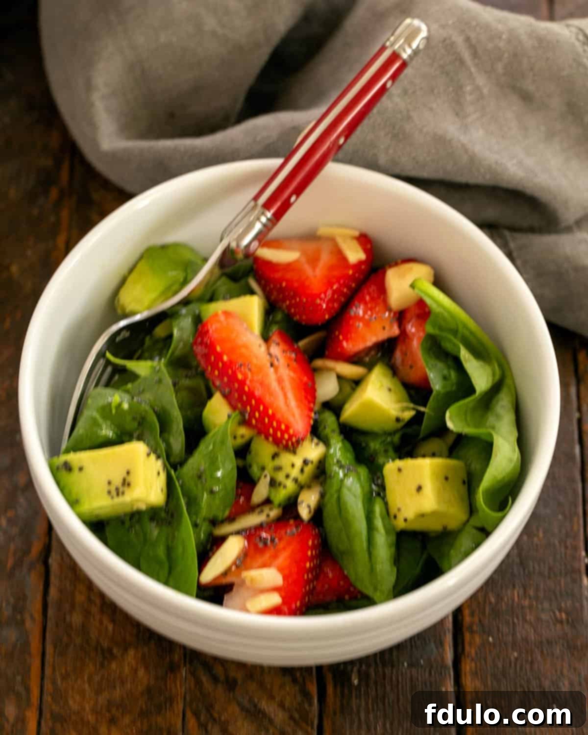An inviting overhead view of a freshly made Strawberry Spinach Salad with Avocados, served in a pristine white salad bowl, ready to be enjoyed.