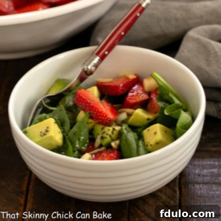 White bowl filled with spinach and strawberry salad with avocados.