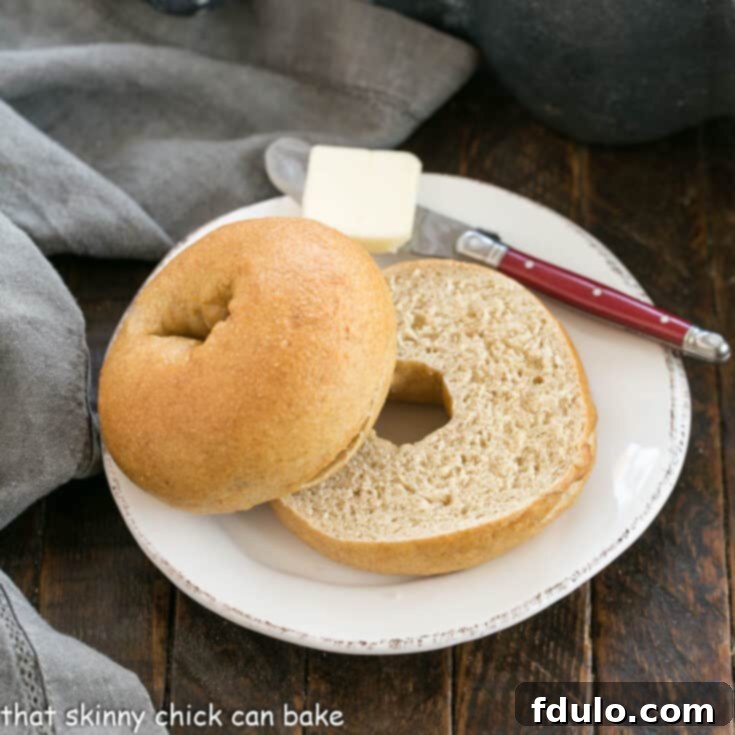 Wholesome Whole Wheat Bagels 2 One Sliced whole wheat bagel on a white plate with a red handle knife topped with a pat of butter
