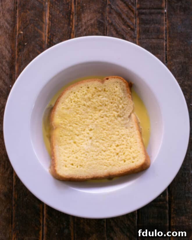 A fully assembled sandwich being carefully dipped into the egg wash mixture.