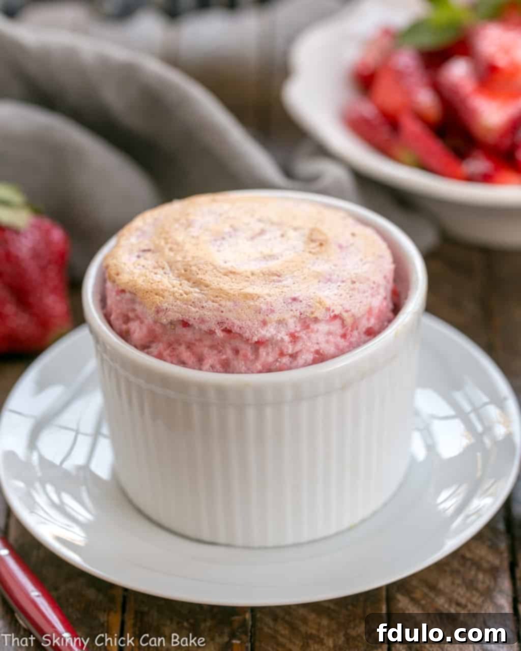 A perfectly baked individual strawberry soufflé, golden brown and dramatically puffed, sitting on a white plate.