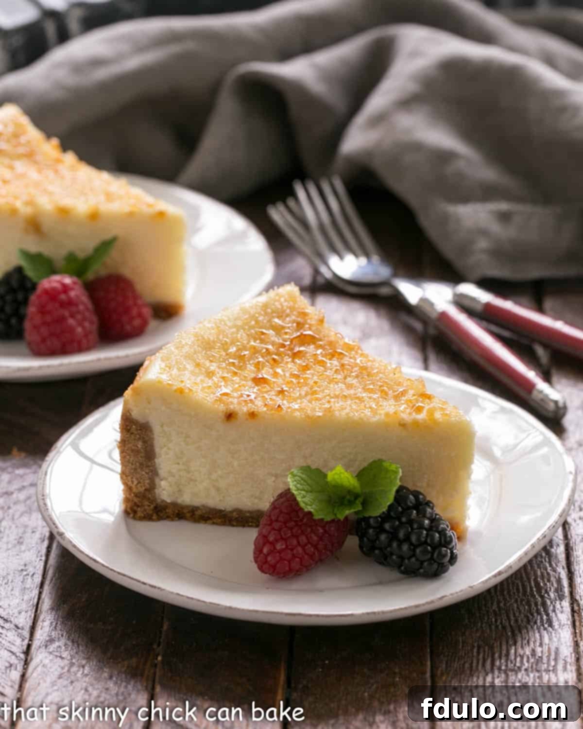 Two slices of creme brulee cheesecake on white plates with berry garnish.
