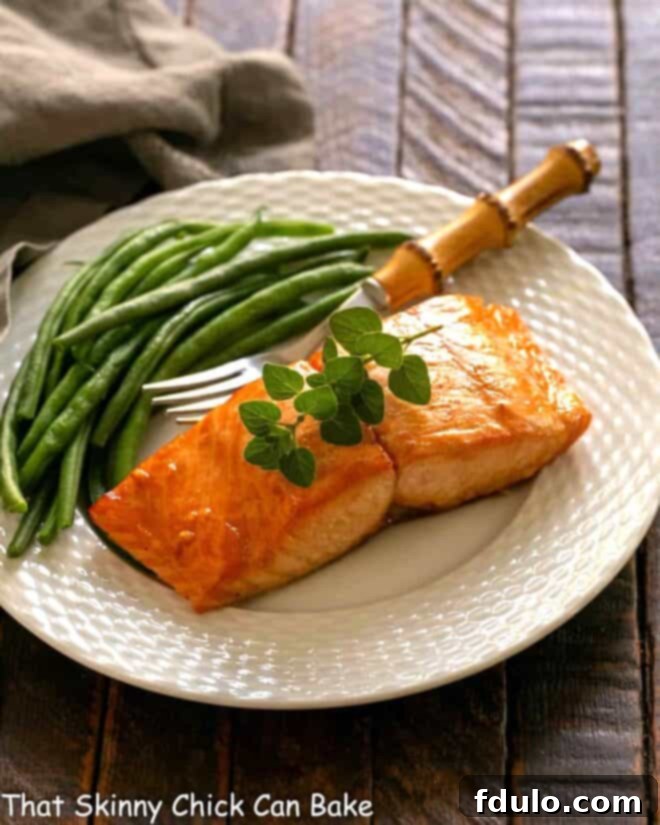 Marinated salmon for two on a white plate with a fork and green beans, showcasing a healthy and delicious meal.