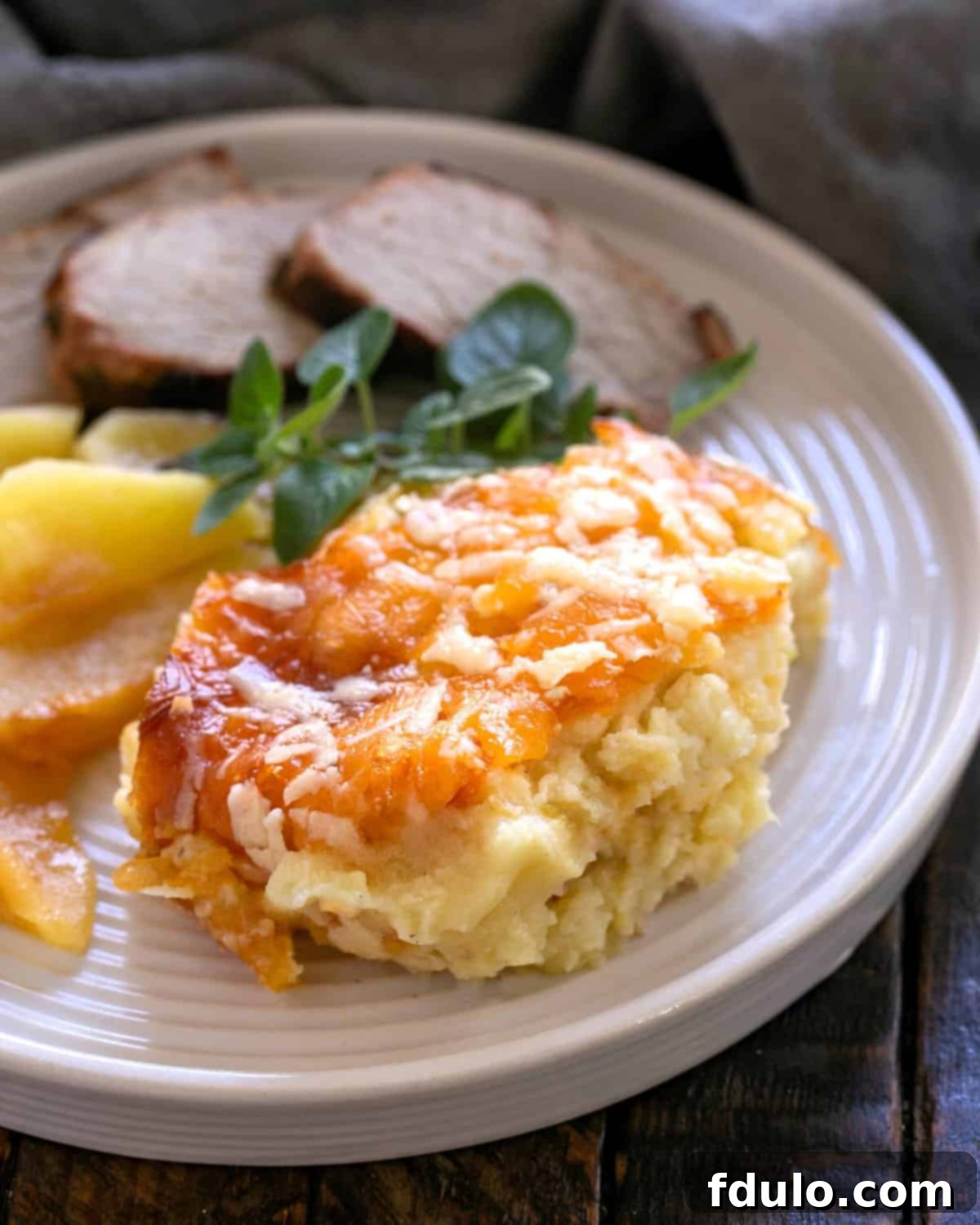 Serving of Twice Baked Potato Casserole on a white dinner plate with pork and apples, showcasing its delicious appeal.