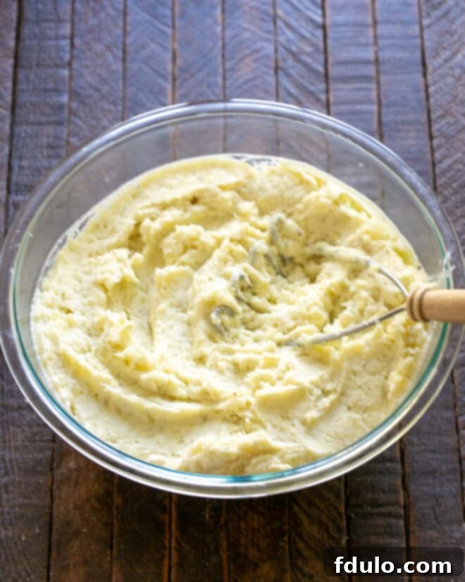 Twice Baked Potato Casserole Step 2: Mashing boiled potatoes with sour cream, heavy cream, salt, and pepper.