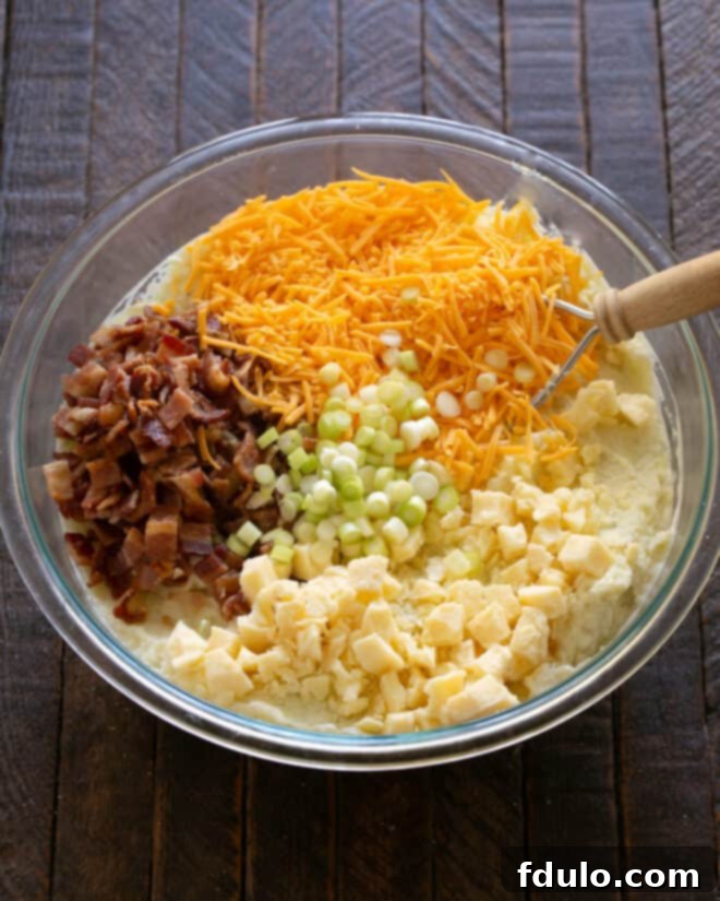 Twice Baked Potato Casserole Step 1: Adding crispy bacon, both cheddar cheeses, and fresh green onions to the mashed potatoes.