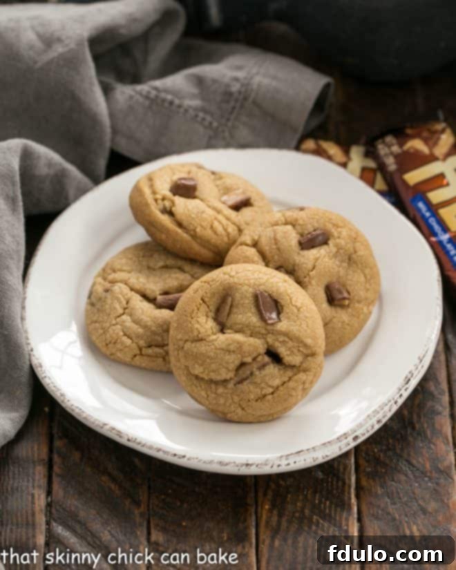 A close-up of four perfectly baked Toffee Biscoff cookies arranged on a pristine white plate, showcasing their golden edges and inviting texture.