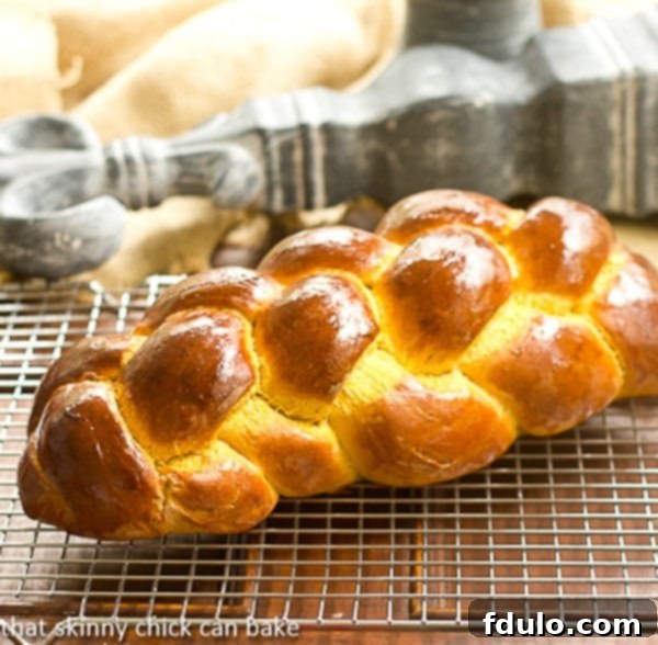 Freshly baked pumpkin challah cooling on a wire rack, showcasing its golden crust and intricate braid.
