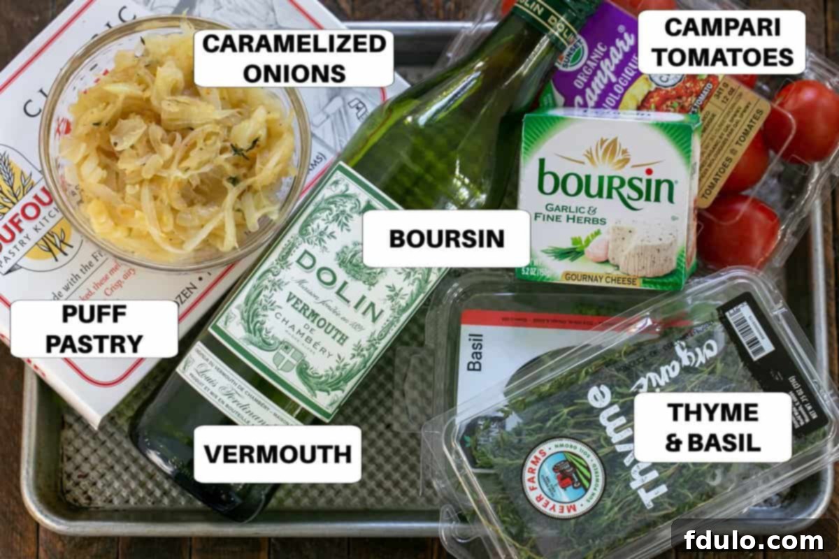 A collection of fresh ingredients for Tomato Boursin Tarts, neatly arranged on a baking sheet, including puff pastry, Boursin cheese, tomatoes, onions, and herbs.