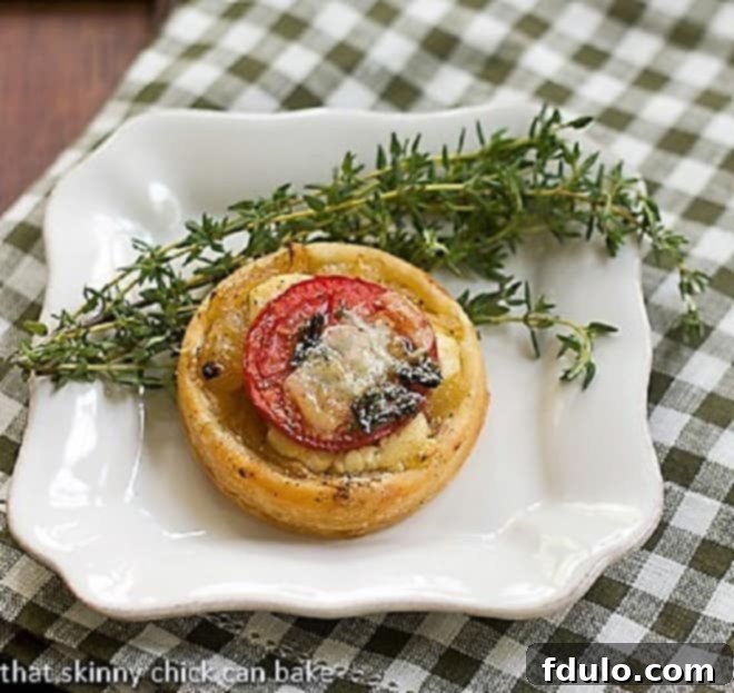 A single Tomato and Boursin Tartlet on a square white plate, garnished with fresh thyme, highlighting its delicate construction and vibrant colors.