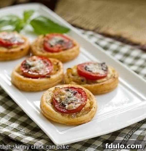 A tray of freshly baked Tomato and Boursin Tartlets, elegantly arranged with a sprig of basil, ready for serving.