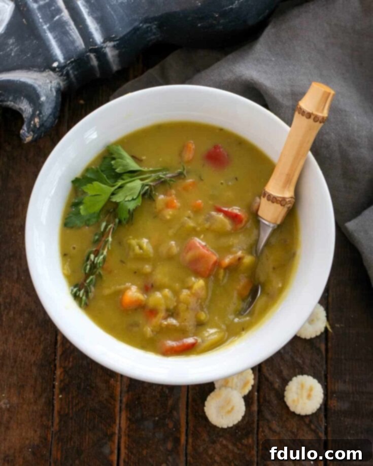 Overhead shot of a rustic white bowl of Split Pea and Ham Soup with a bamboo handle spoon, garnished with fresh herbs.