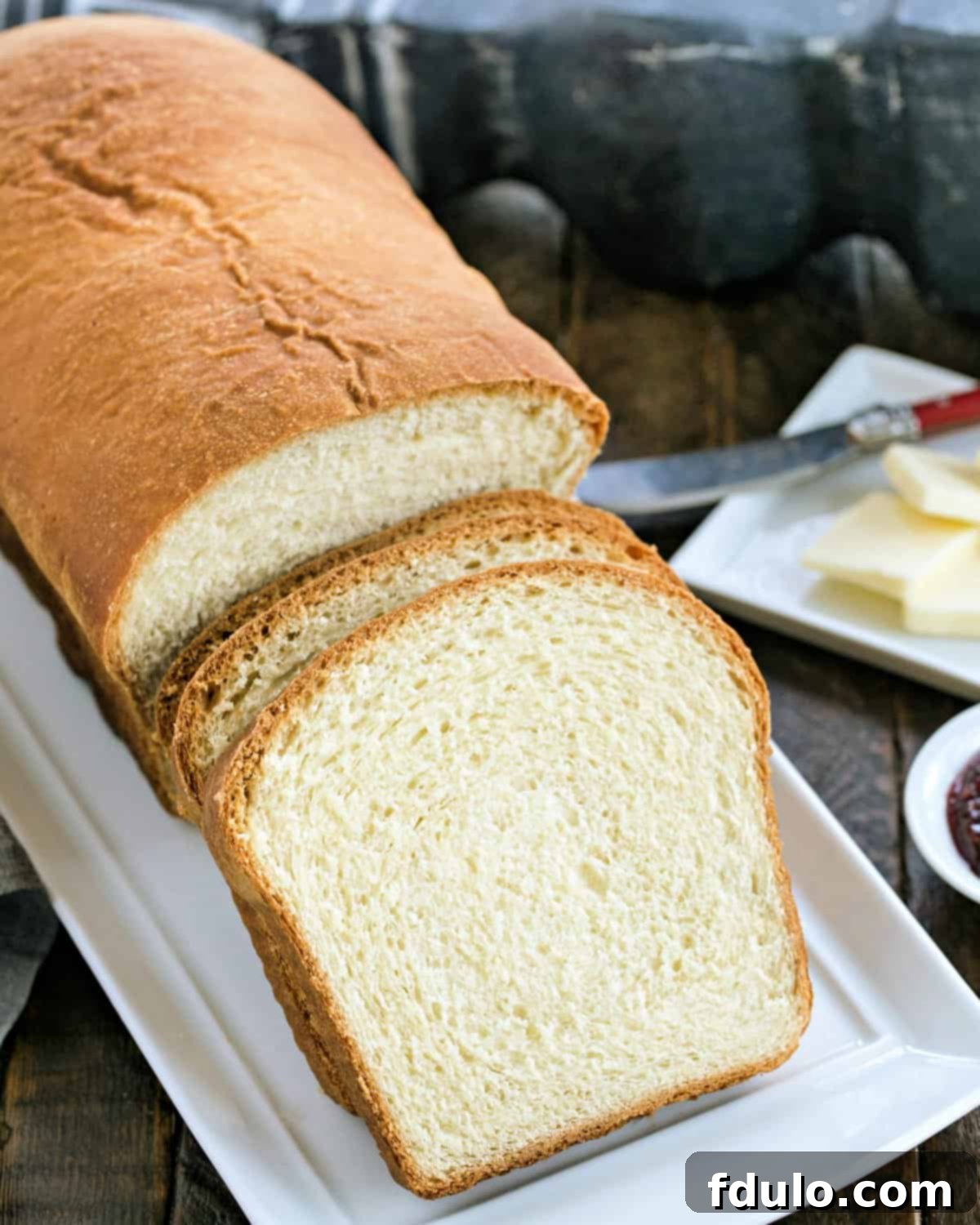 A freshly baked loaf of homemade potato bread sitting on a white ceramic platter, ready to be sliced.