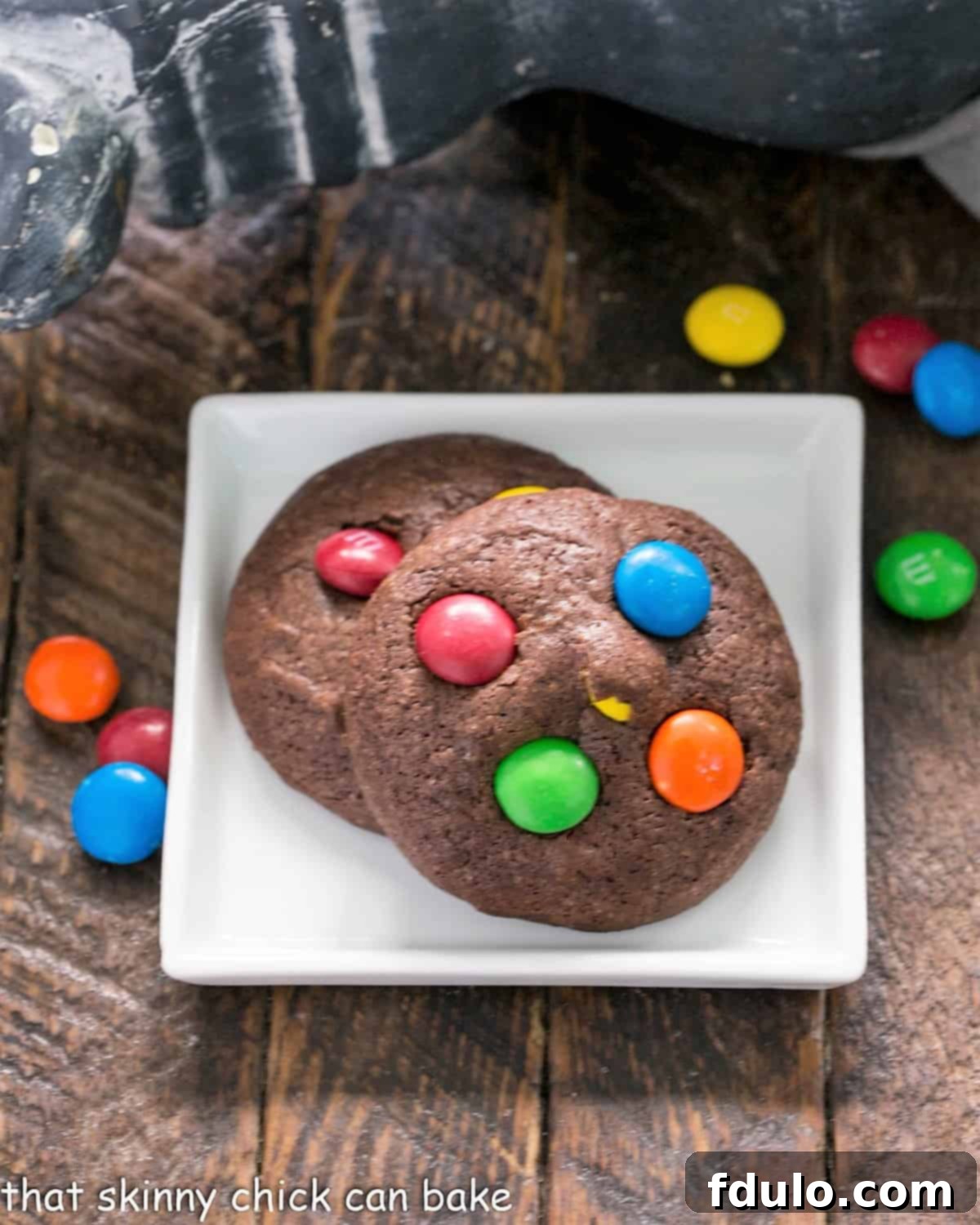 Two soft and fudgy M&M Brownie Cookies resting on a small white plate, showcasing their inviting texture and colorful candy bits.