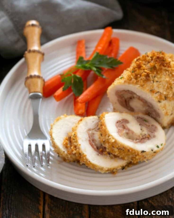 Chicken Cordon Bleu partially sliced on a white plate with carrots and a fork.