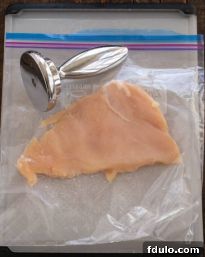 Step 1: Pounding a boneless, skinless chicken breast between two sheets of plastic wrap with a meat mallet, creating a thin, even cutlet for the Cordon Bleu.