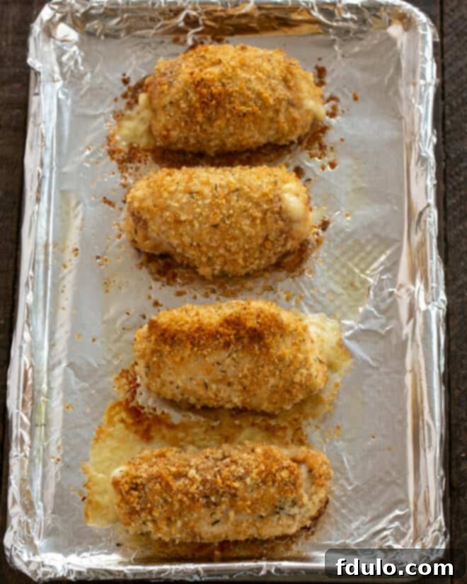 Step 7: Several breaded chicken cordon bleu rolls arranged neatly on a baking sheet, ready to be placed into the oven for baking until golden and cooked through.