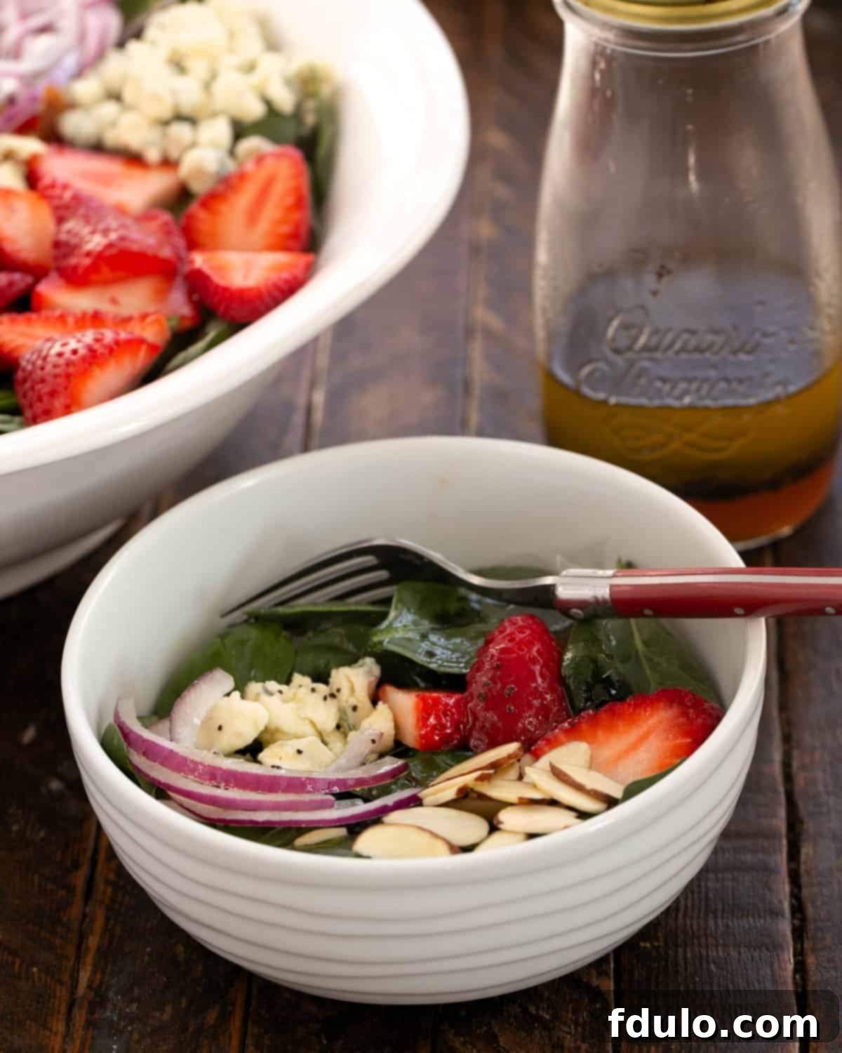 Small bowl filled with strawberry spinach salad in front of the serving bowl.