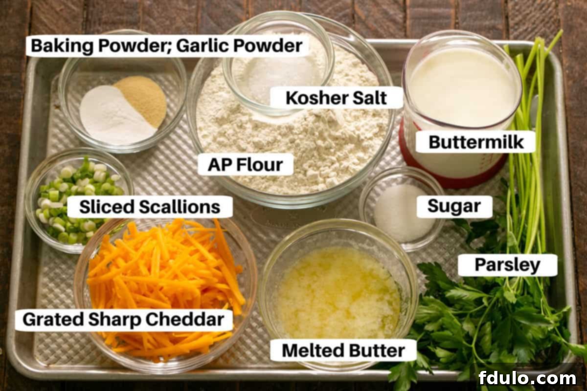 A colorful array of ingredients for cheddar herb biscuits, including flour, shredded cheese, scallions, parsley, and buttermilk, neatly arranged on a baking sheet, ready for preparation.