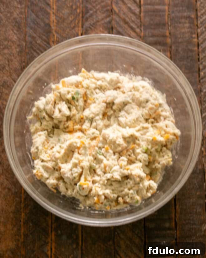 Buttermilk, shredded cheddar cheese, sliced green onions, and chopped parsley being added to the dry ingredients in a mixing bowl, ready to be gently stirred.