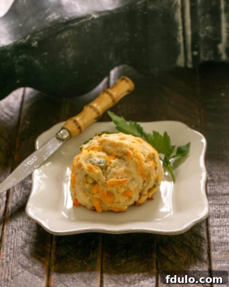 A cheddar biscuit on a white plate with a sprig of parsley and a knife.