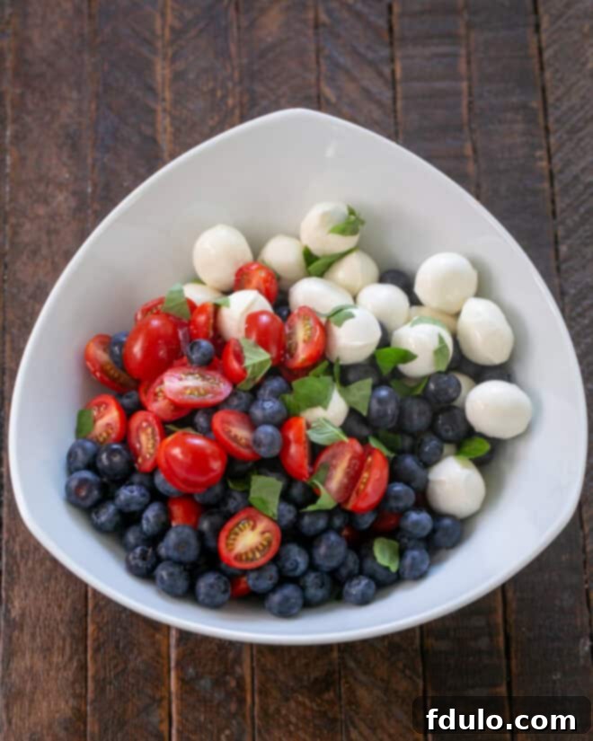 Blueberry Bliss Caprese 5 Salad ingredients, including blueberries, tomatoes, and mozzarella, neatly arranged in a bowl, ready to be tossed with dressing.