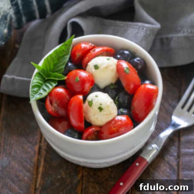 Blueberry Bliss Caprese 6 A freshly tossed Caprese Salad with Blueberries, garnished with vibrant green basil leaves, presented in a white serving bowl.