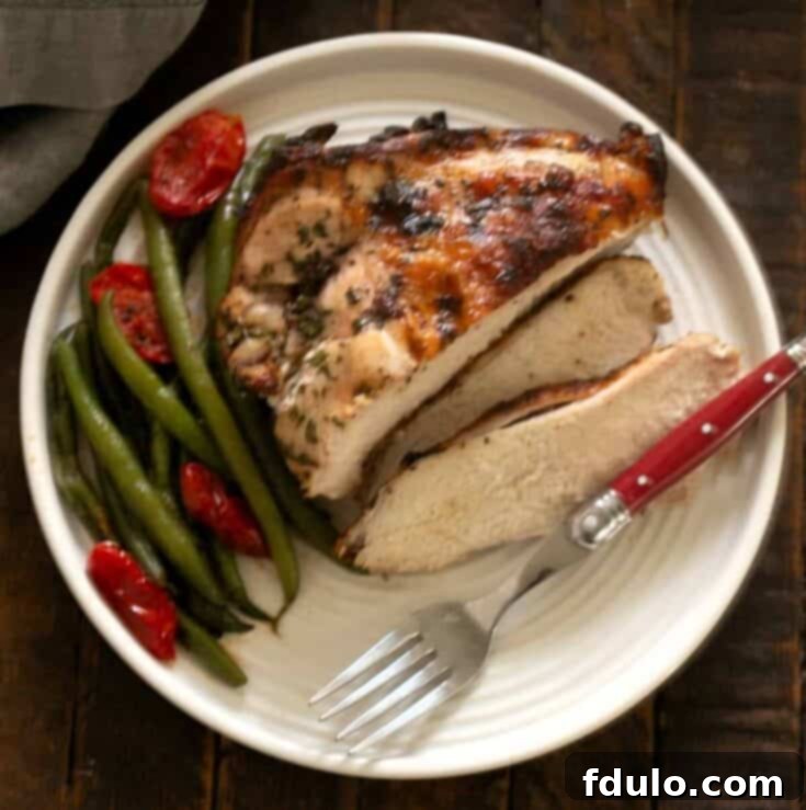 Overhead view of sliced chicken piccata on a white plate with a fork and green beans.