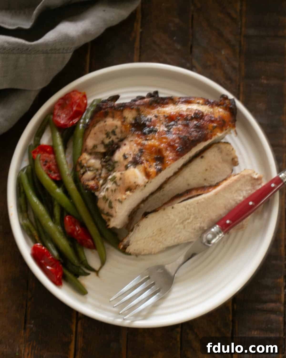 Easy Chicken Piccata Recipe on a dinner plate with a fork, showing sliced chicken and green beans.
