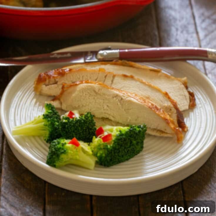 Slices of buttermilk brined chicken on a white plate with a knife and broccoli.