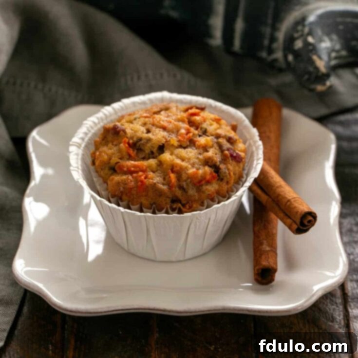 Morning glory muffin on a small white plate with cinnamon sticks.