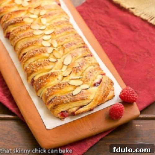 Freshly baked Raspberry Danish Braid cooling on a wooden cutting board.