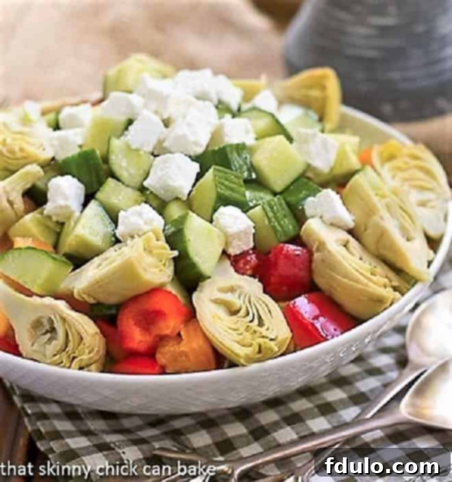 Greek Salad with Feta in a white salad bowl with silver serving spoon and fork, ready to be enjoyed.