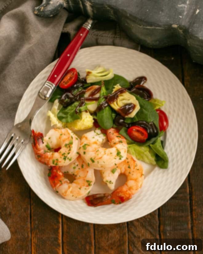 A close-up of a plated Shrimp Scampi dish, showing the succulent shrimp glistening with garlic butter sauce, served with a fresh salad and a fork.